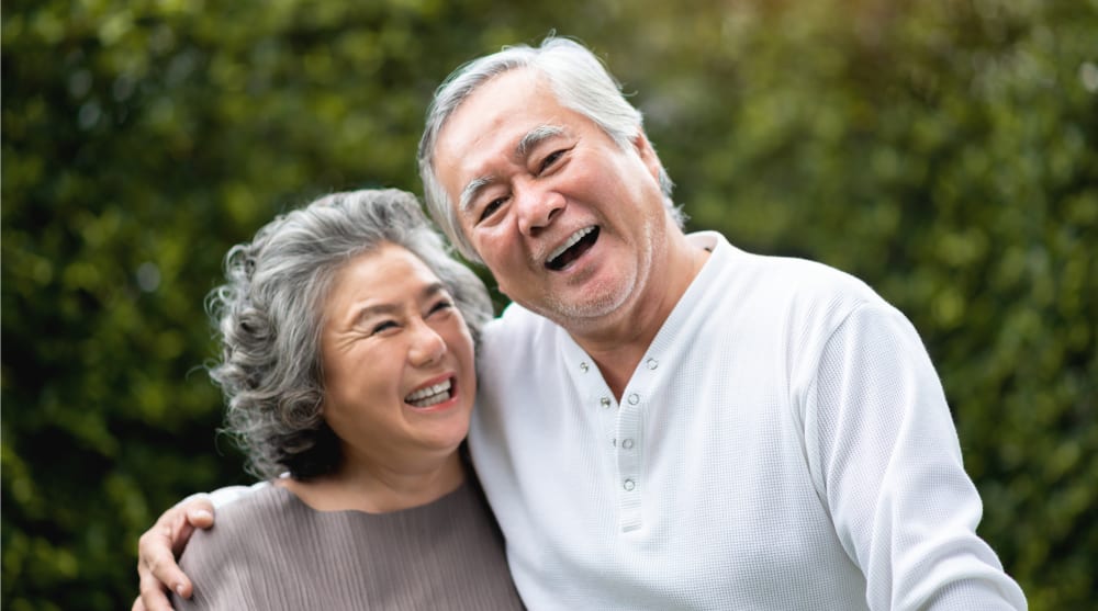 An older couple laughs while standing outside.